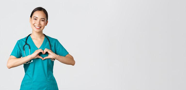 Arbeitnehmer im Gesundheitswesen, Pandemie-Konzept. SchÃ¶ne fÃ¼rsorgliche asiatische Ã„rztin, weibliche Krankenschwester in Kitteln, die Herzgeste zeigt und lÃ¤chelt, die sich mit Liebe um Patienten kÃ¼mmert.