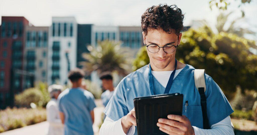 Junger Mann in medizinischer Kleidung nutzt ein Tablet zur digitalen Hygieneschulung im Freien