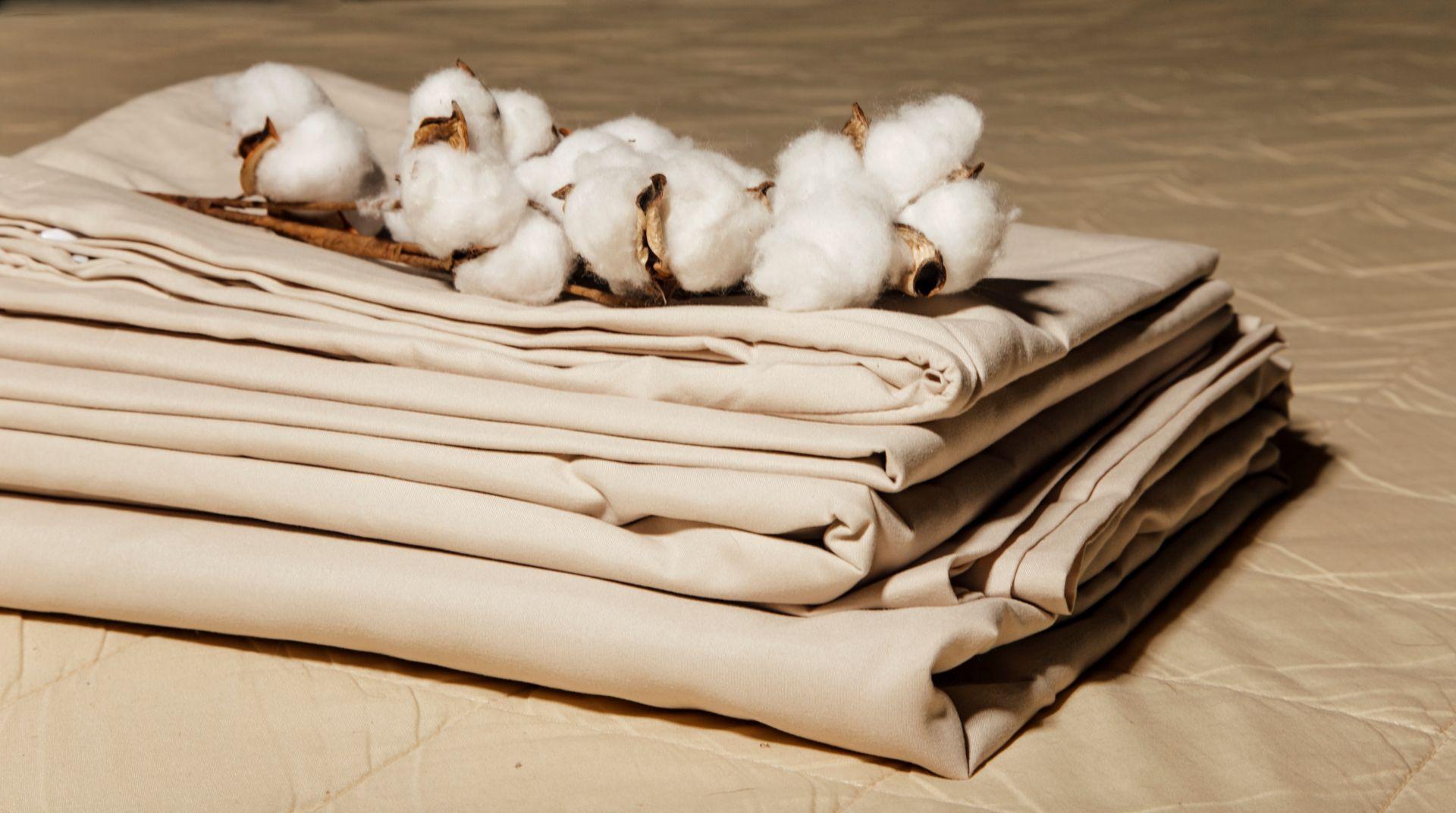 Gestapelte Bio Bettwaesche in Beige mit Baumwollzweigen als Symbol fuer Naturmaterial